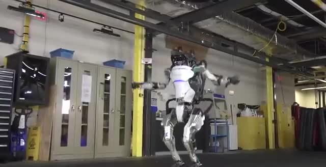 A white and silver humanoid robot with its arms out in a workshop.