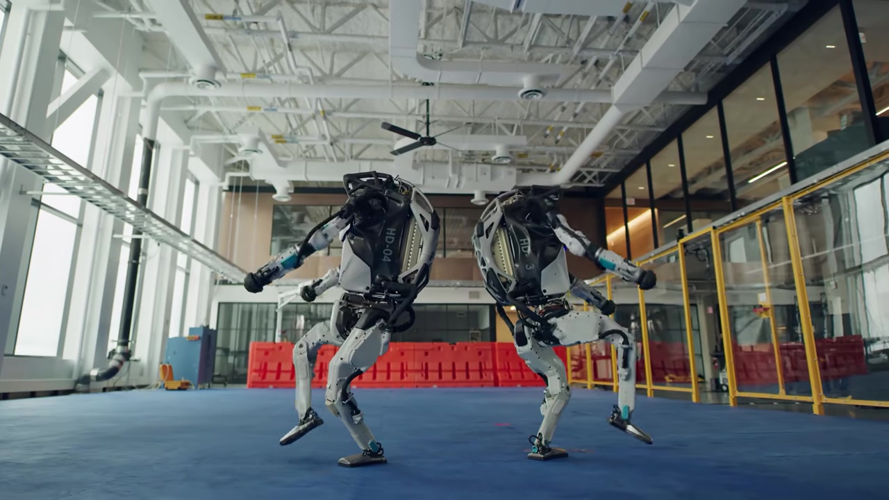 Two Boston Dynamics Atlas robots posing mid-dance on a blue floor