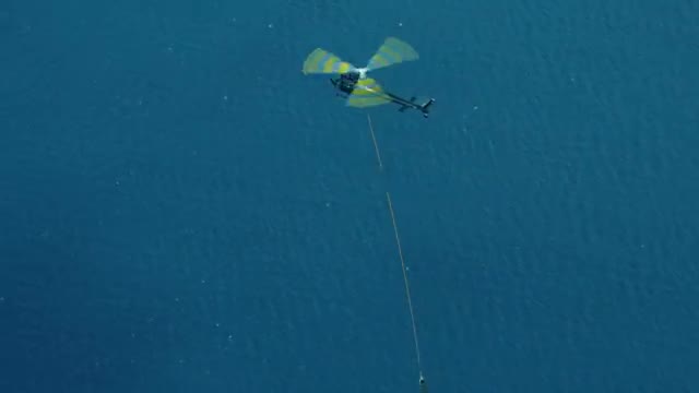 Helicopter trailing a hook toward a descending parachute over the sea