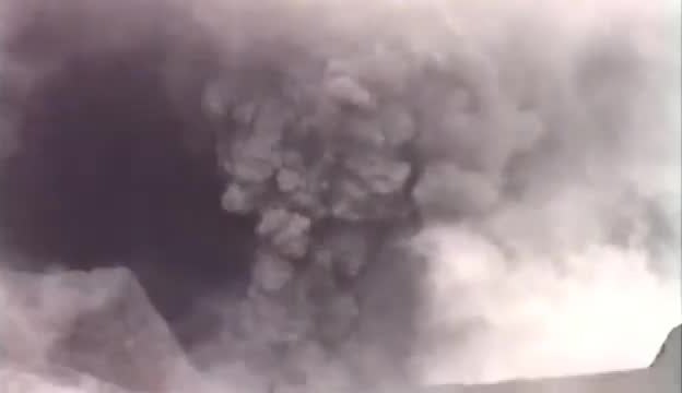 A grey ash and steam plume rising from a volcanic crater.