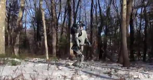 A humanoid robot walking through snow between bare trees.