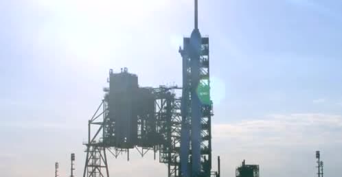 A Falcon 9 standing on the pad beside its launch tower.