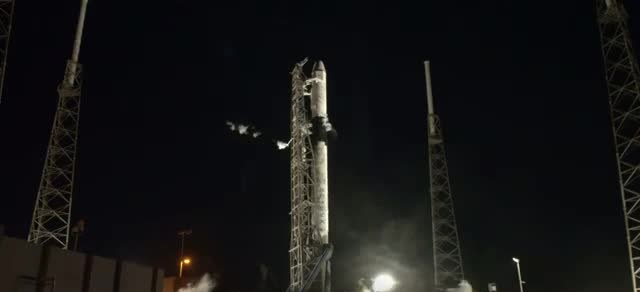 Falcon 9 standing on the pad at night between two lightning towers before the CRS-20 launch