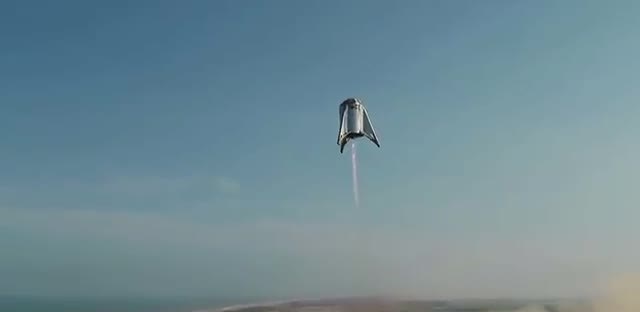 A short stainless-steel rocket prototype climbing with a pale exhaust plume.