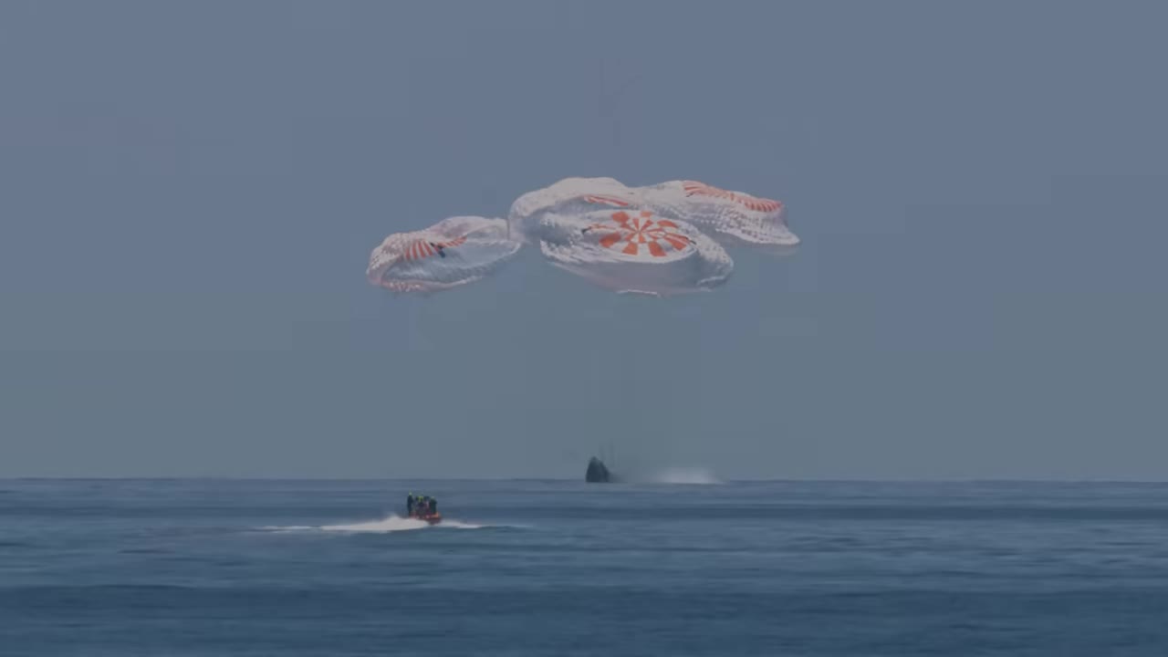 Crew Dragon under four parachutes descending toward boats on the ocean