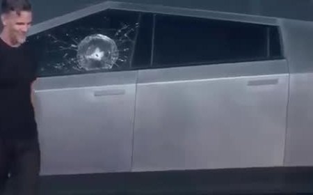 A steel ball's impact spidering the side window of a stainless-steel truck.