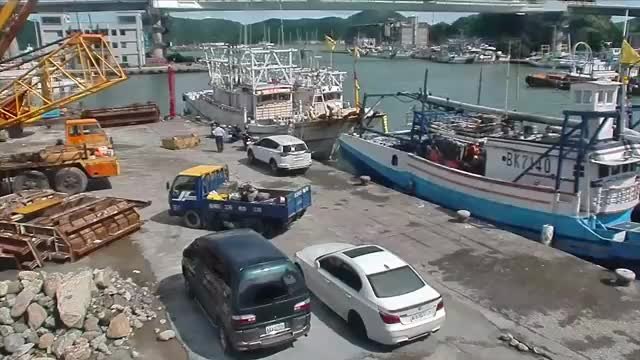 A harbour with fishing boats under a concrete bridge, filmed from above.