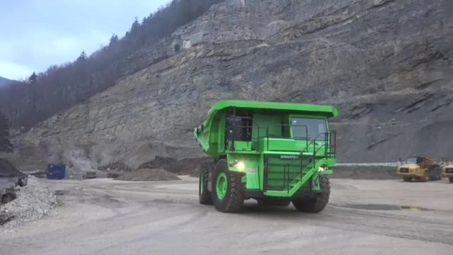 A large green electric mining truck on a quarry road.