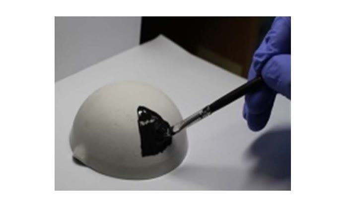 A gloved hand brushing black paint onto a white dome.