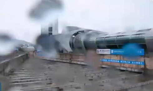 A long grey terminal building sliding along a prepared track, dust rising beside it.
