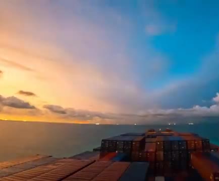 Container stacks on a ship at sea under a sunset sky