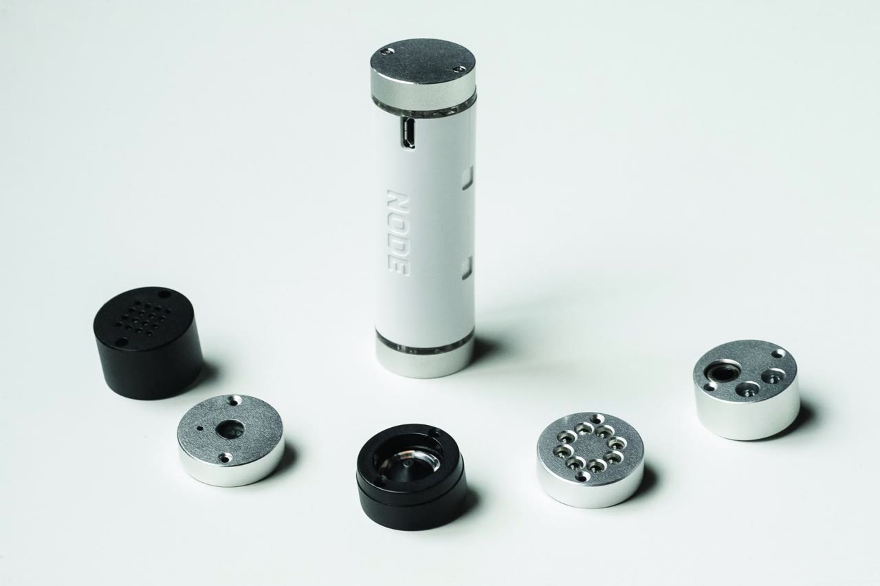 A white cylinder surrounded by round metal and black sensor caps.