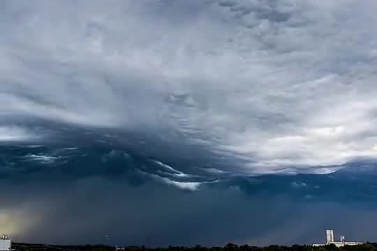 A dark rolling wave of cloud over a low skyline.