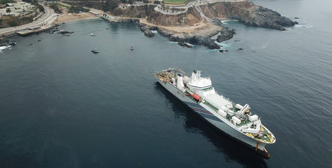 Cable ship floats a yellow-buoyed fiber cable toward shore