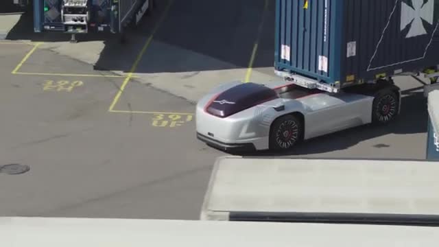 A cabless autonomous truck pulling a shipping container in a port yard