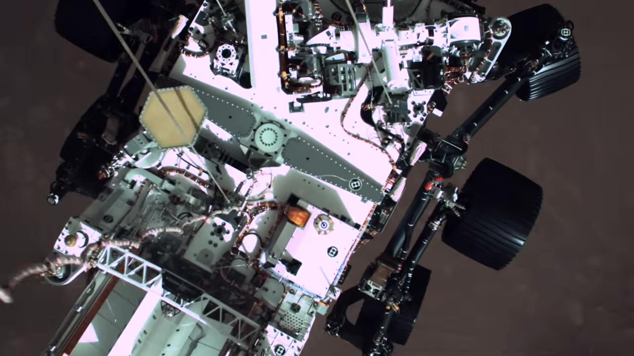Top-down view of Perseverance rover hanging from skycrane cables over Mars
