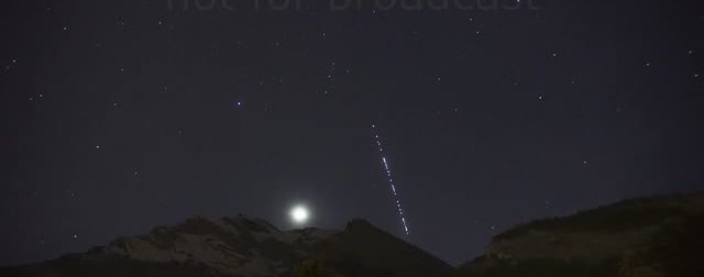 Line of Starlink satellites rising over a moonlit mountain ridge