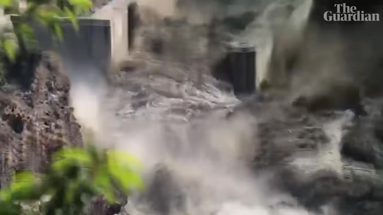 Turbulent floodwater surging through a concrete dam in a mountain valley