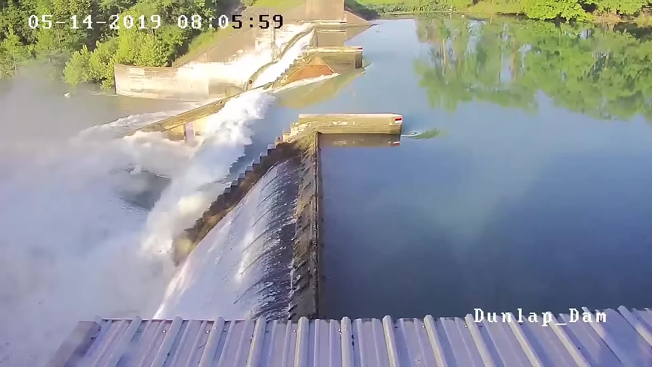 Brown floodwater surging through a breached gate at Dunlap Dam
