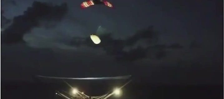 Falcon fairing half under a parafoil descending toward a ship’s net at night