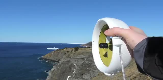 A small white water turbine held up above a rocky coast.