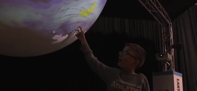 Person standing beside a large glowing sphere used as a data display