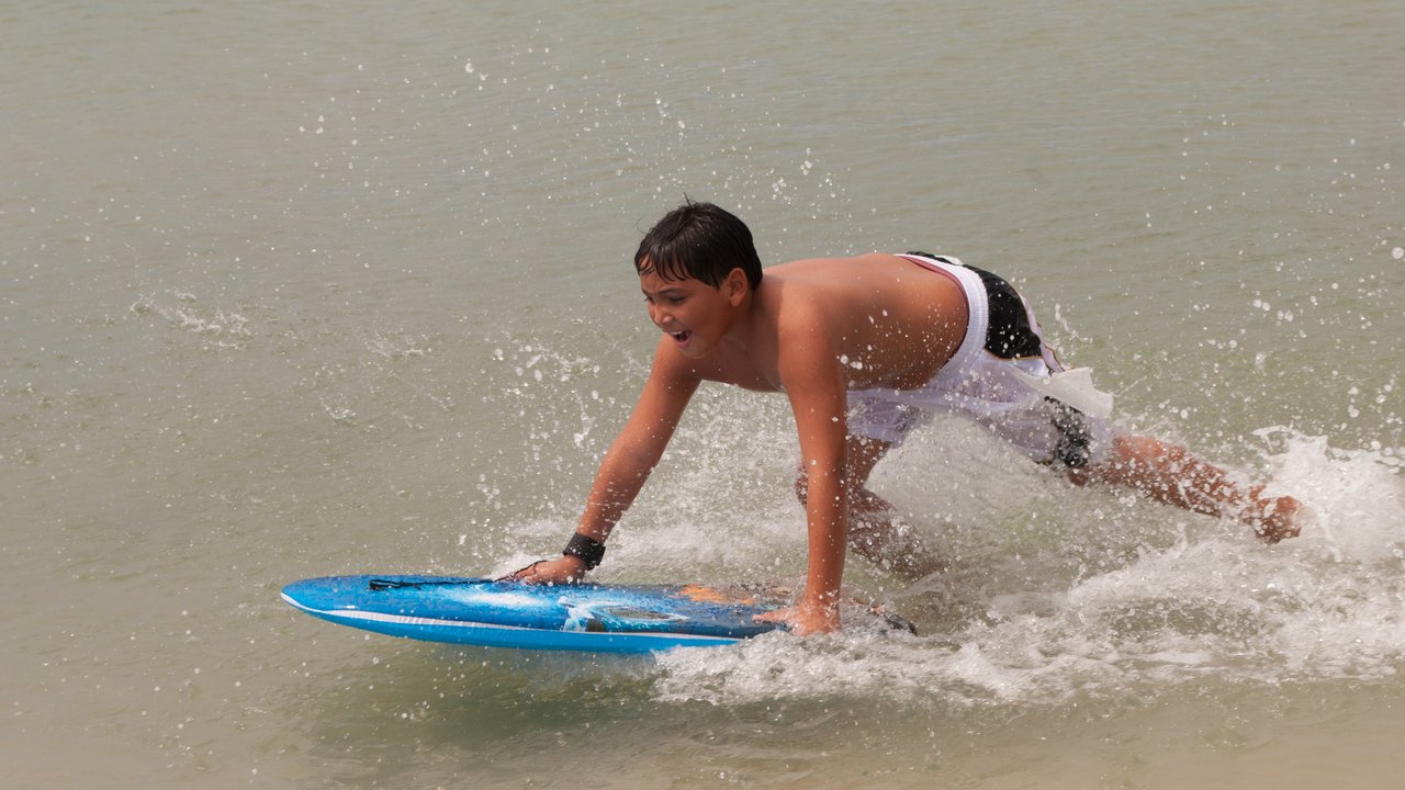 A boy riding a blue bodyboard through shallow surf on a beach.